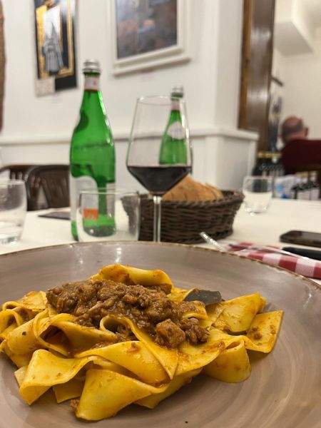 Pappardelle al ragù servite in tavola con il bicchiere di vino accanto