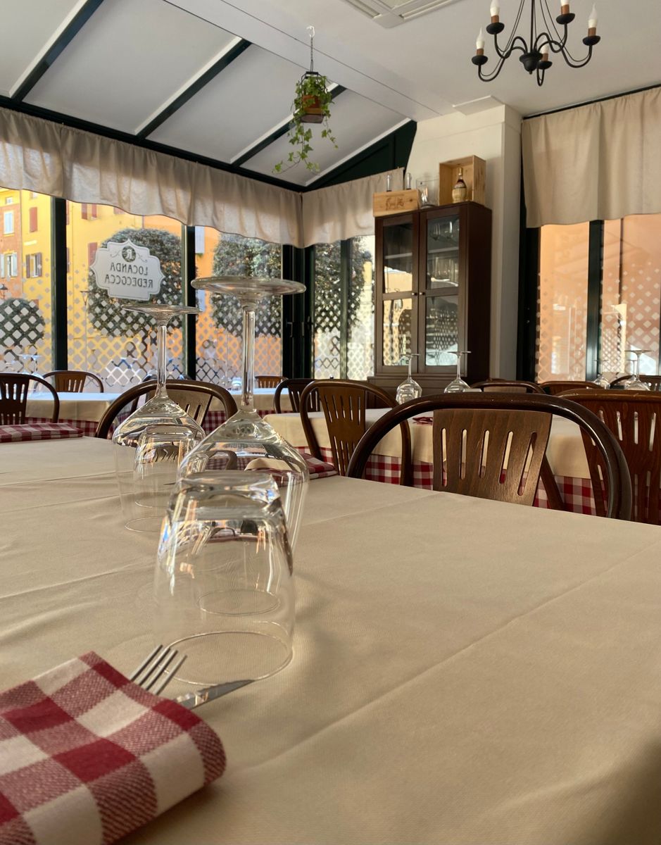La veranda della Locanda Redecocca affacciata sulla piazzetta, con tovaglie a quadri e finestre luminose